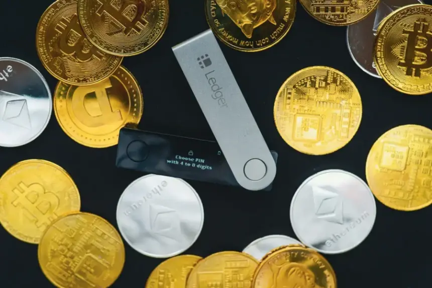 一枚 Ledger 硬件钱包放在深色表面上，周围环绕着金币和银币。